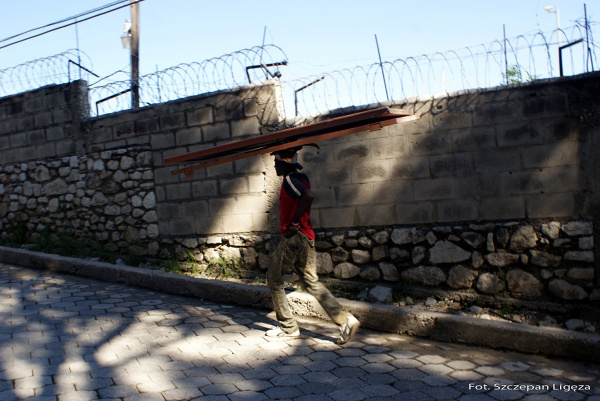 Haitańczyk niosący drzwi. Za murem osiedle pracowników organizacji międzynarodowych